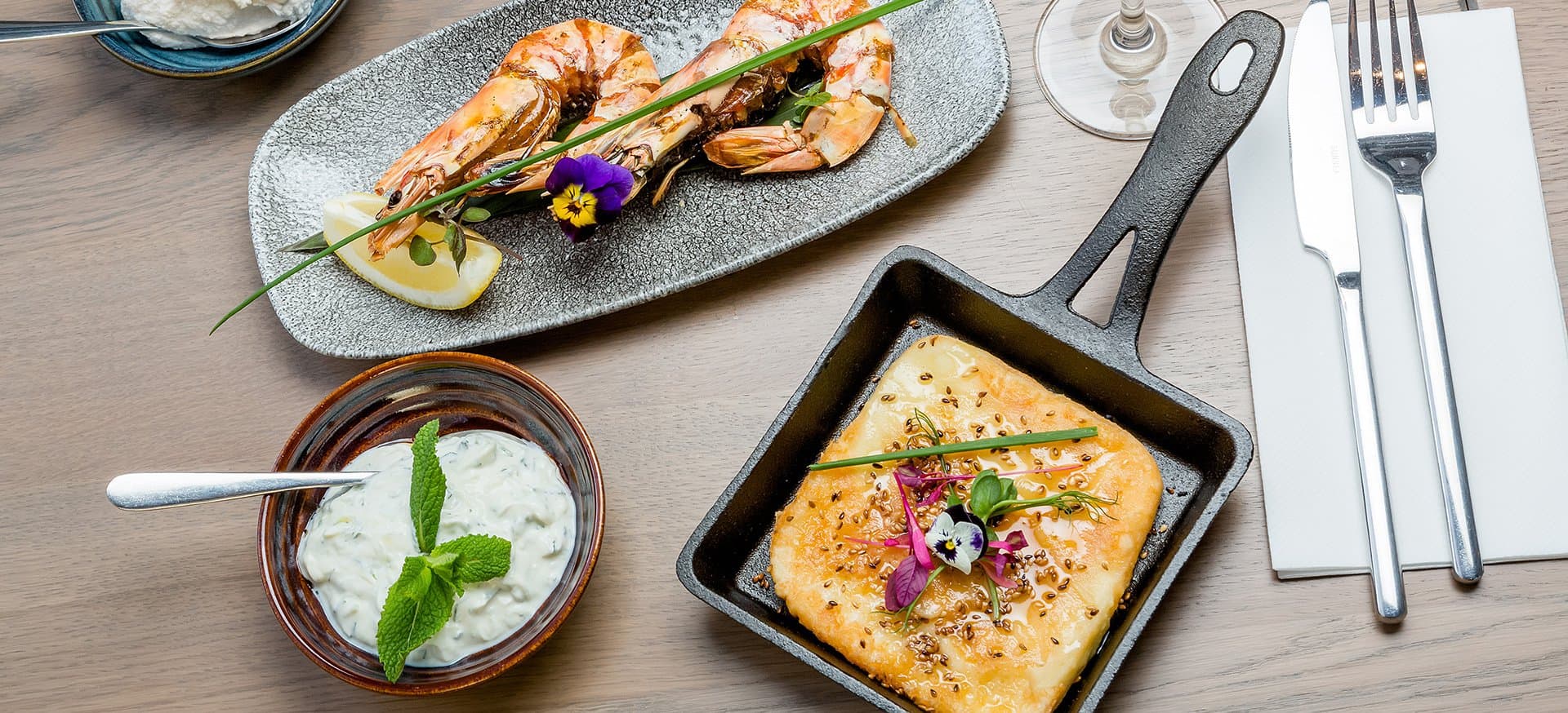 Charcoal grilled king prawns, saganaki and tzatziki laid across the table